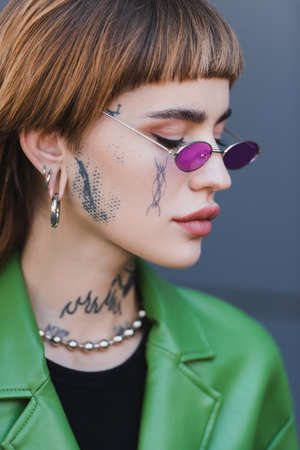 close up view of tattooed woman in piercing and stylish eyeglasses outdoorsの写真素材