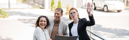realtor with folder pointing away near happy husband and african american wife, banner