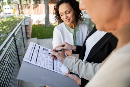 blurred man signing loan application near african american wife and realtor