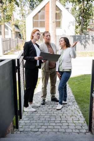 african american woman pointing away near husband and realtor with folder