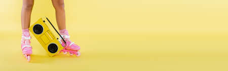 cropped view of african american woman in roller skates near retro boombox on yellow, banner