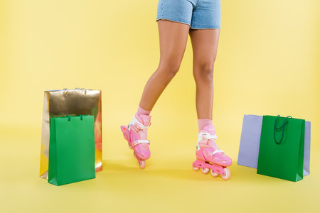 cropped view of african american woman in roller skates near shopping bags on yellow
