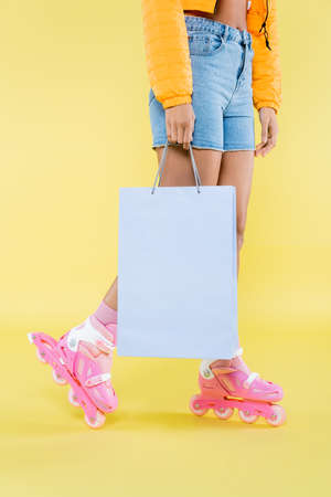 cropped view of african american young woman on roller skates holding shopping bag on yellow