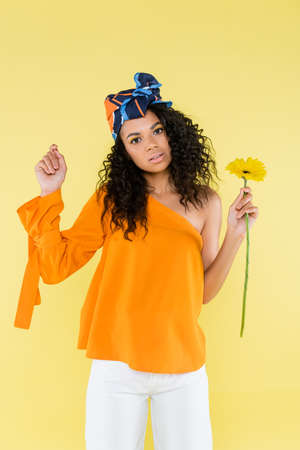 african american woman with bare shoulder holding flower isolated on yellow