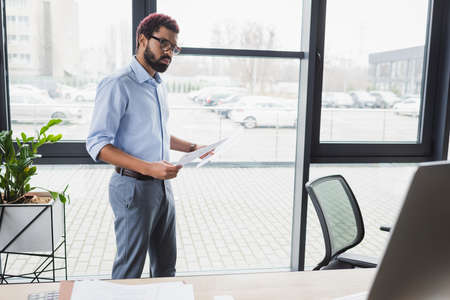 African american businessman holding documents near computer in office