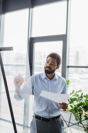 African american businessman with document writing on glass board in office