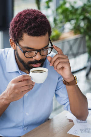 African american businessman in eyeglasses holding cup of coffee in officeの写真素材