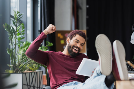 Excited african american businessman showing yes gesture while using digital tablet in officeの写真素材