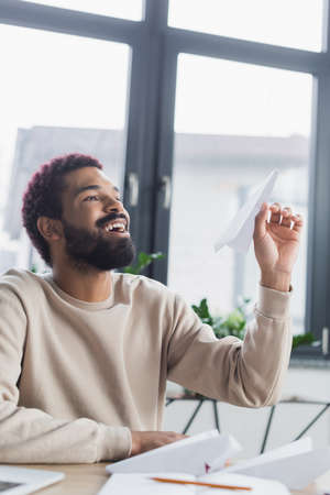 Smiling african american businessman holding paper plane in office