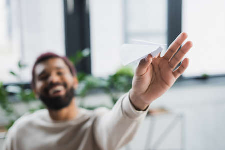 Paper plane in hand of blurred african american businessman in officeの写真素材