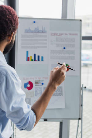 African american businessman holding pen near blurred flip chart in office