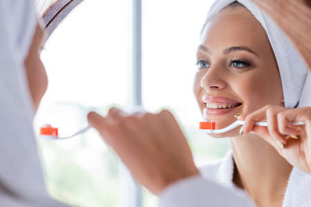 cheerful woman brushing teeth and looking at mirrorの写真素材