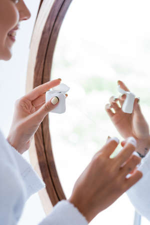 cropped view of cheerful woman holding dental floss near mirror