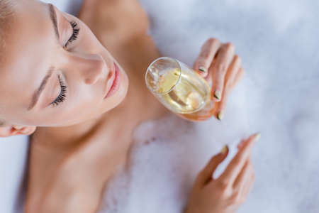 top view of woman taking bath and holding glass of champagne