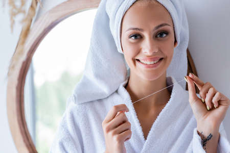 tattooed and happy woman holding dental floss in bathroom