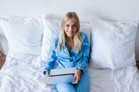 high angle view of cheerful young woman in pajamas with laptop looking at cameraの写真素材