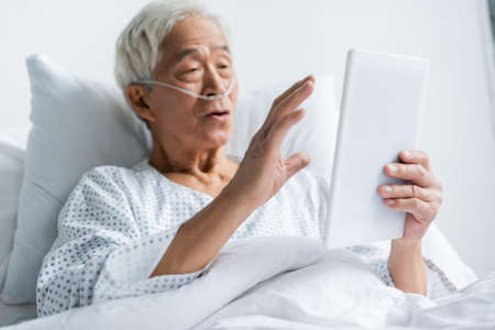 Digital tablet in hand of blurred asian patient with nasal cannula in hospital ward