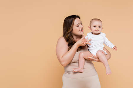 Happy plus size woman holding hand of child isolated on beigeの写真素材
