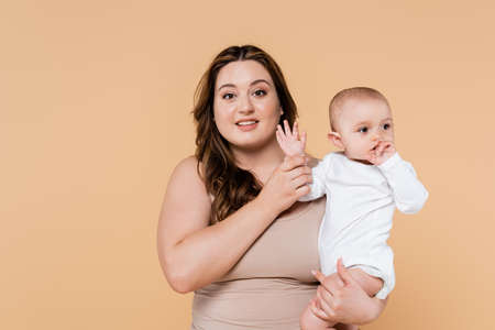 Smiling plus size parent holding hand of baby daughter isolated on beigeの写真素材