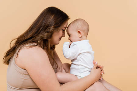 Side view of woman with overweight holding baby daughter isolated on beigeの写真素材