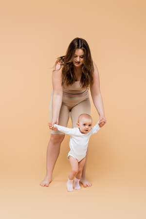 Plus size woman walking near baby daughter on beige backgroundの写真素材