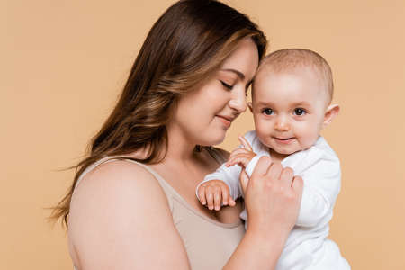 Brunette woman with closed eyes holding baby isolated on beige
