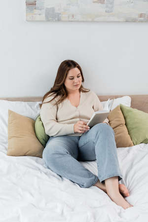 Brunette woman with overweight reading book on bedの写真素材