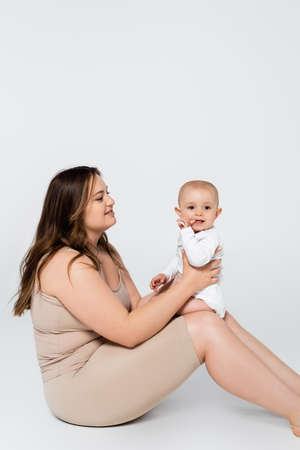 Pretty plus size woman holding child with finger near mouth on grey backgroundの写真素材