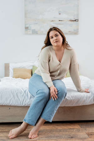 Pretty body positive woman in casual clothes looking at camera on bedの写真素材
