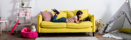 preteen girl lying on sofa and using laptop in modern living room, bannerの写真素材
