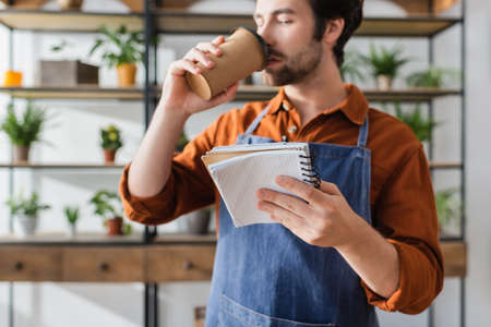 Notebook in hand of blurred seller drinking coffee in flower shopの写真素材
