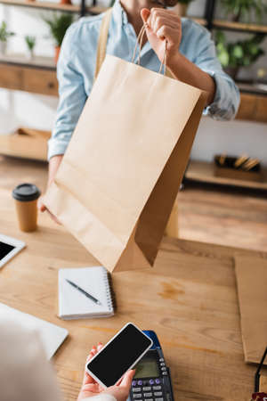 Cropped view of florist holding shopping bag near customer paying with smartphone in flower shopの写真素材
