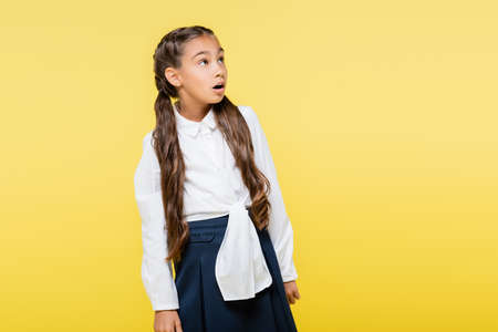 Astonished pupil in shirt looking away isolated on yellow