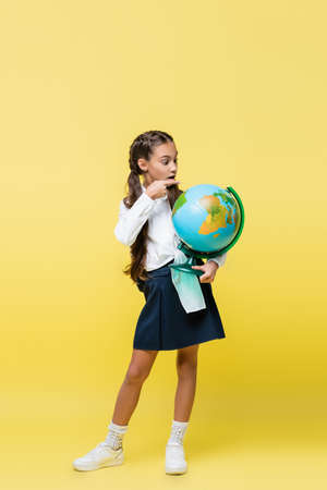 Full length of schoolgirl pointing at globe on yellow backgroundの写真素材