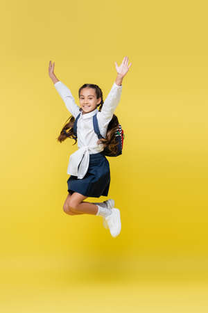 Cheerful schoolgirl with backpack jumping on yellowの写真素材