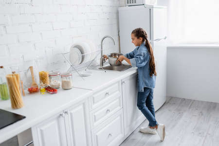 Side view of kid pouring water in saucepan in kitchen