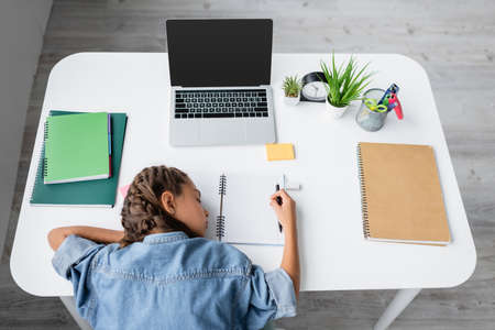 Top view of kid sleeping near copy books and laptop with blank screen on table