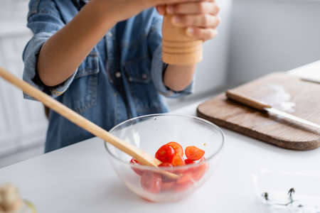 Cropped view of blurred kid seasoning cherry tomatoes in bowl while cooking in kitchenの写真素材