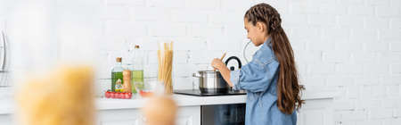 Child cooking near saucepan on stove and ingredients in kitchen, bannerの写真素材