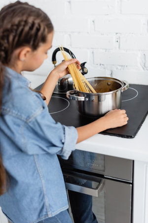 Blurred kid pouring spaghetti in saucepan on stove in kitchenの写真素材