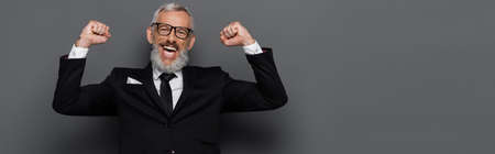 excited middle aged man in suit and glasses rejoicing on gray, banner