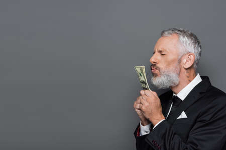 tattooed middle aged businessman kissing dollar banknotes isolated on gray