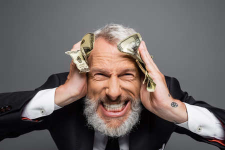 insane middle aged businessman holding dollar banknotes and grinning isolated on grayの写真素材