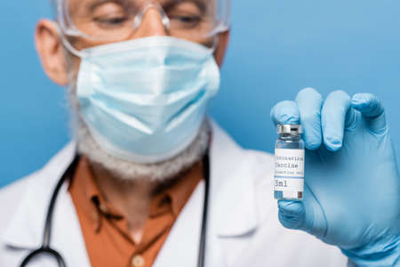 blurred doctor in medical mask and latex glove holding vial with coronavirus vaccine lettering...