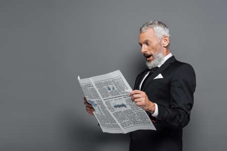 shocked middle aged man in suit reading newspaper on grayの写真素材