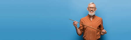 happy middle aged teacher in glasses holding pointer stick on blue, bannerの写真素材