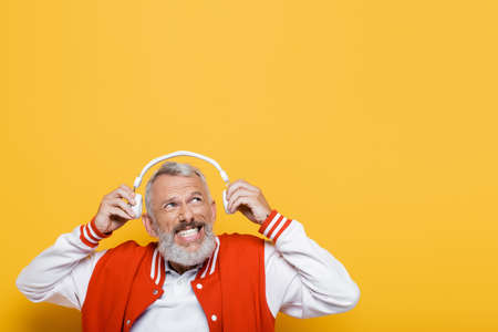 positive middle aged man holding wireless headphones isolated on yellow