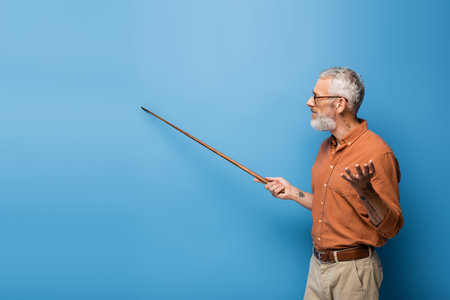tattooed middle aged teacher in glasses holding pointer stick and gesturing on blueの写真素材