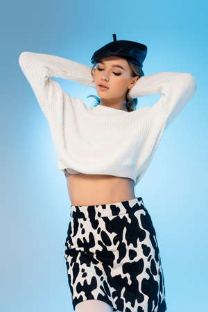 young woman in beret, sweater and skirt with cow print posing on blueの写真素材