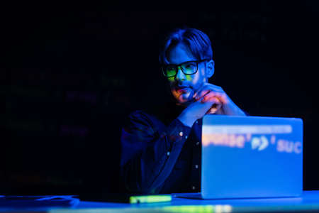 Developer in eyeglasses sitting near computer with code reflection in office isolated on black